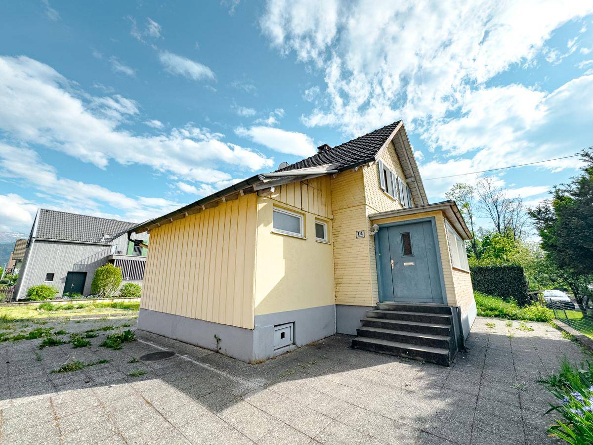 Seitenansicht des Einfamilienhauses mit gelber Fassade, Treppe und gepflasterter Fläche.