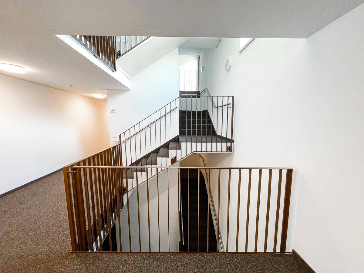 Modernes Treppenhaus mit mehreren Etagen, schlichten Geländern und Teppichboden in den Fluren.