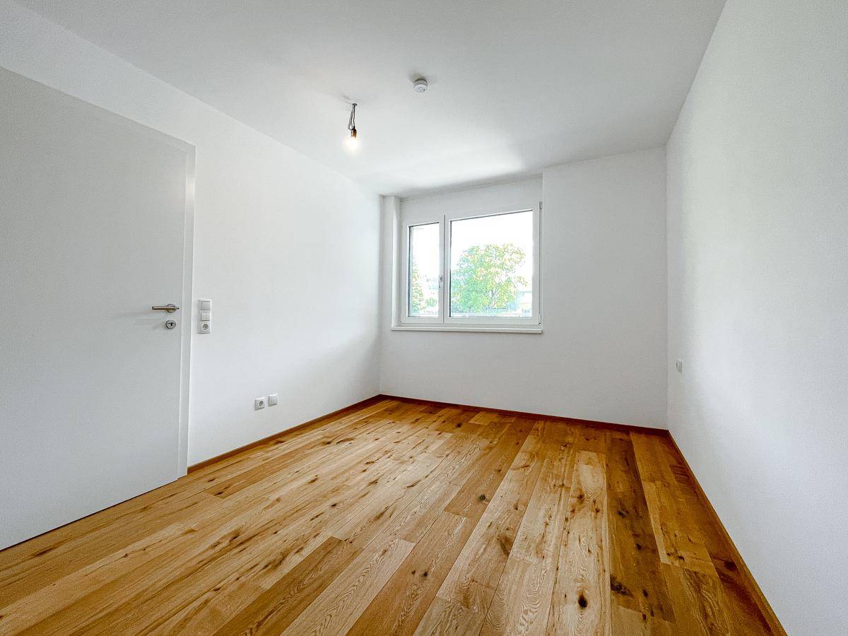 Ruhiges Schlafzimmer mit warmem Holzparkett und einem Fenster, das den Blick ins Grüne freigibt.