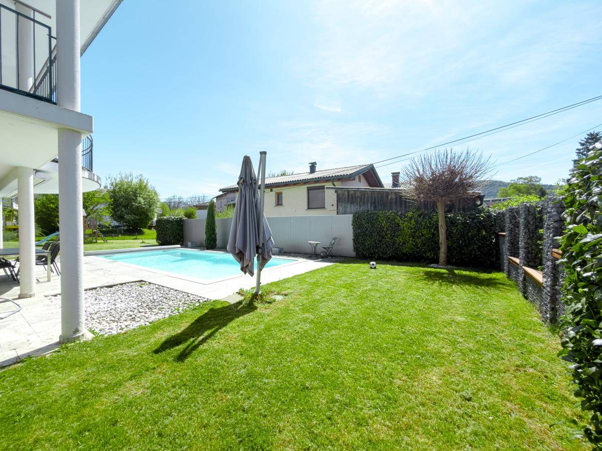Gepflegter Garten mit Rasenfläche, Pool und Sonnenschirm neben dem Haus.
