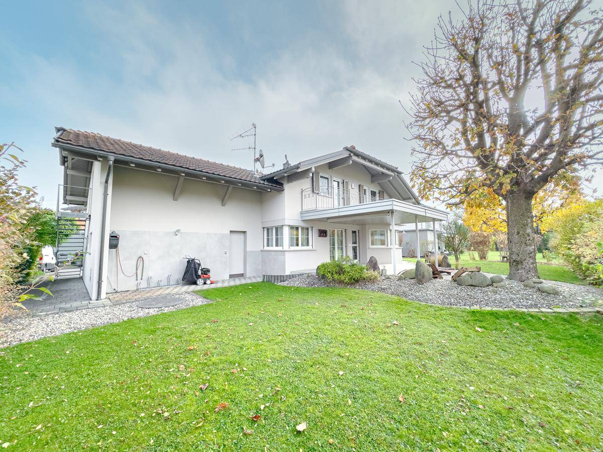 Rückansicht des Hauses mit weitläufigem Garten, überdachter Terrasse und Außentreppe.