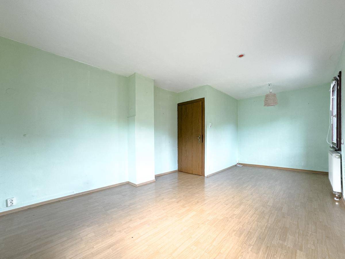 Leeres Wohnzimmer mit hellgrünen Wänden und Laminatboden, bereit zur individuellen Gestaltung.