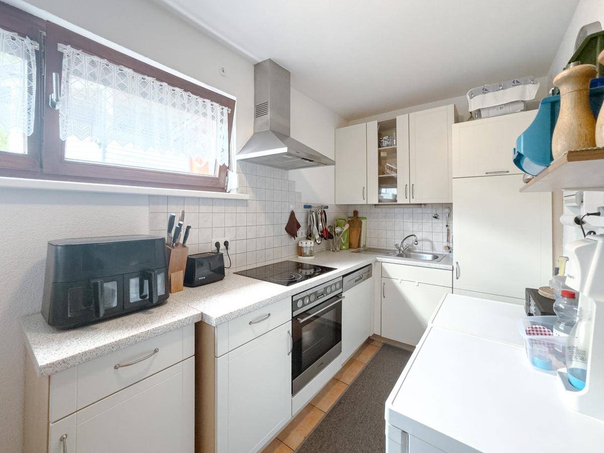 Funktionale Küche mit weißen Schränken, Induktionskochfeld und Fenster für Tageslicht.