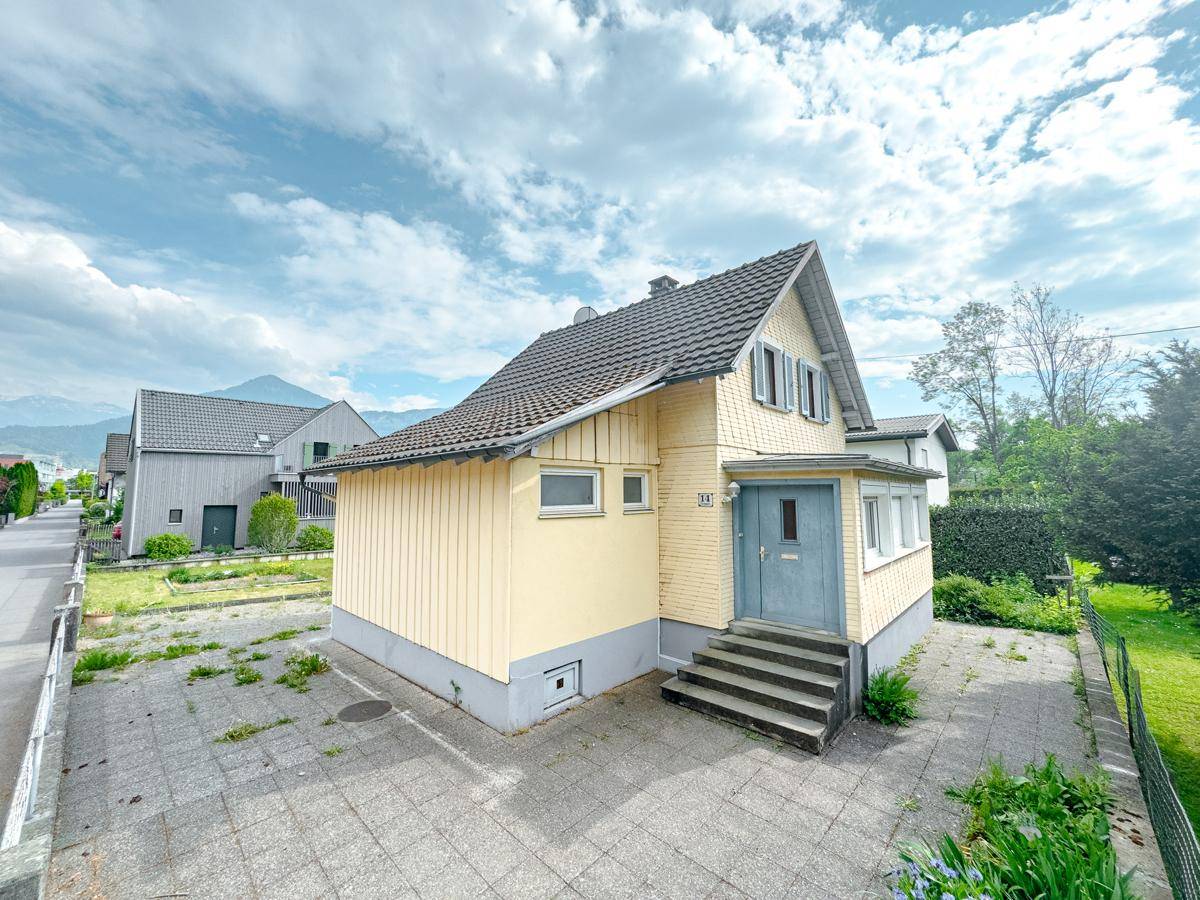 Vorderansicht des Einfamilienhauses mit gelber Fassade, Treppe und gepflasterter Auffahrt.