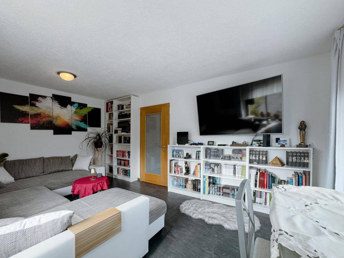 Geräumiges Wohnzimmer mit großem Fernseher, Bücherregalen und gemütlichem Ecksofa.