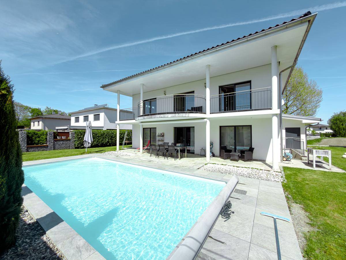 Weitläufiger Poolbereich mit gepflasterter Terrasse und Blick auf das moderne Haus.