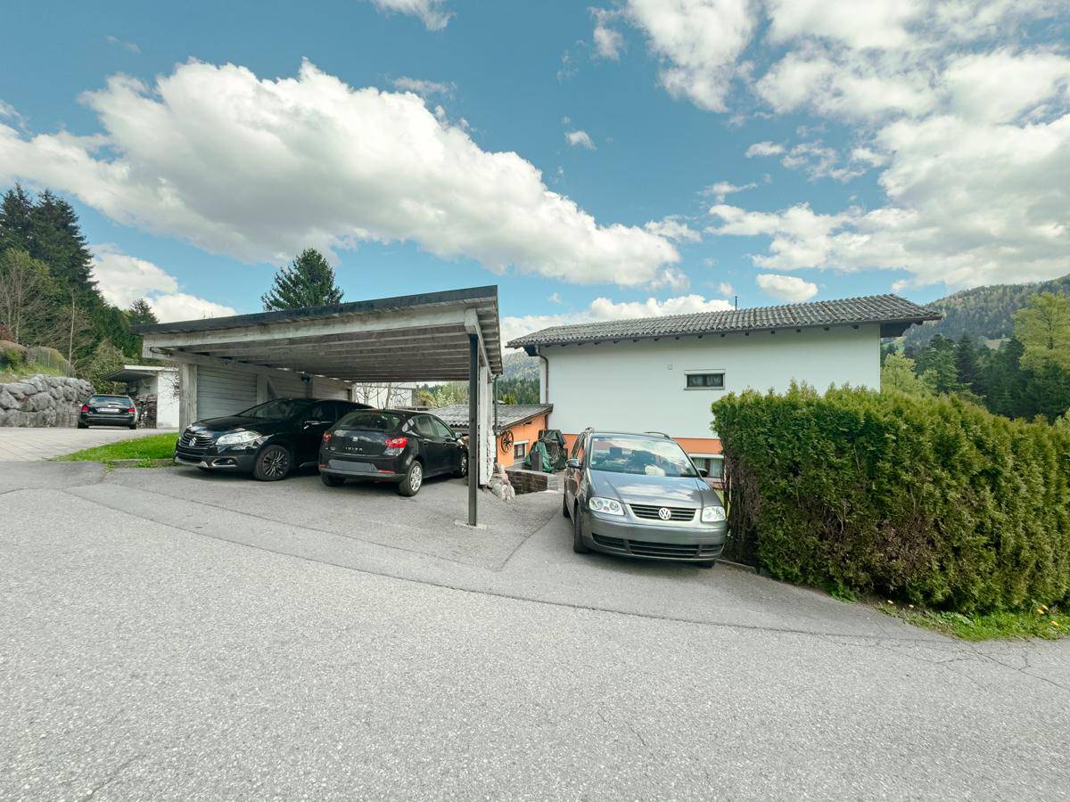 Carport und Außenstellplätze vor dem Haus, umgeben von grüner Hecke und Bäumen.