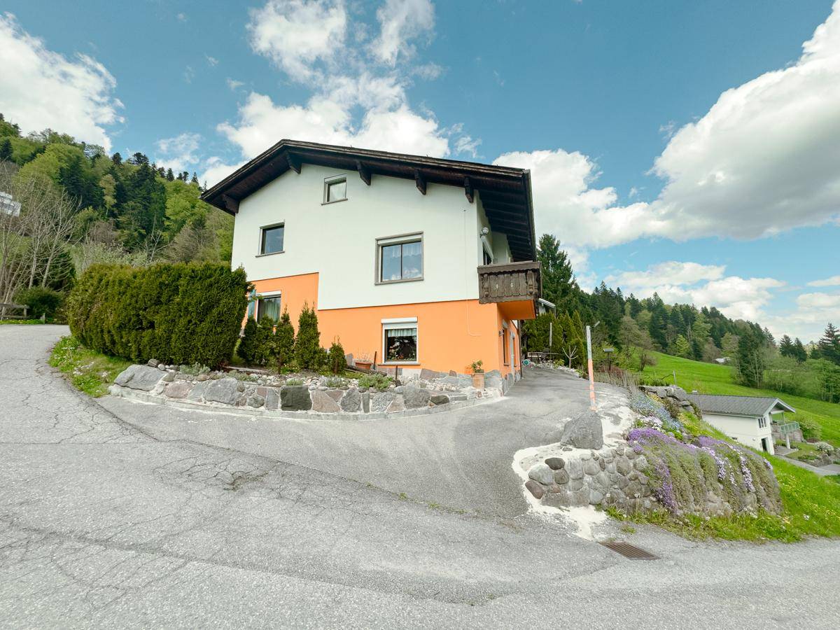 Ansicht des Hauses von der Straße, eingebettet in die Hanglage mit grüner Umgebung.