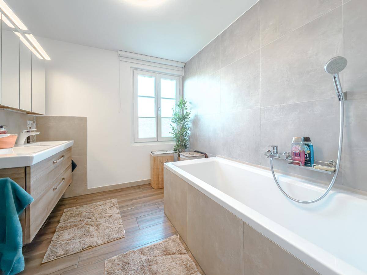 Modernes Badezimmer mit Badewanne, großformatigen Fliesen und Fenster für Tageslicht.