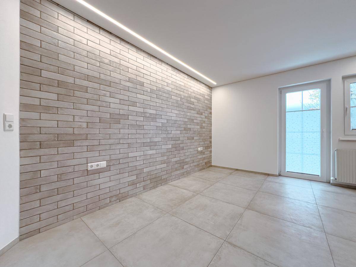 Moderner Raum mit Ziegelwand, Fliesenboden und indirekter Deckenbeleuchtung.
