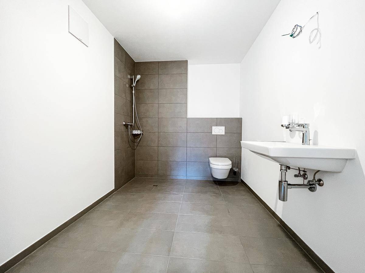 Modernes Badezimmer mit ebenerdiger Dusche, Wand-WC und großformatigen grauen Fliesen.