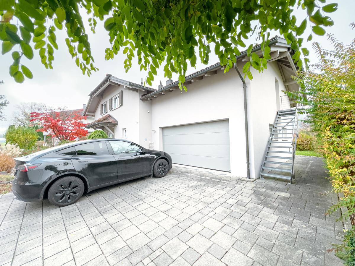Ansicht der Garage und Einfahrt mit einem geparkten Auto, umgeben von Bäumen.