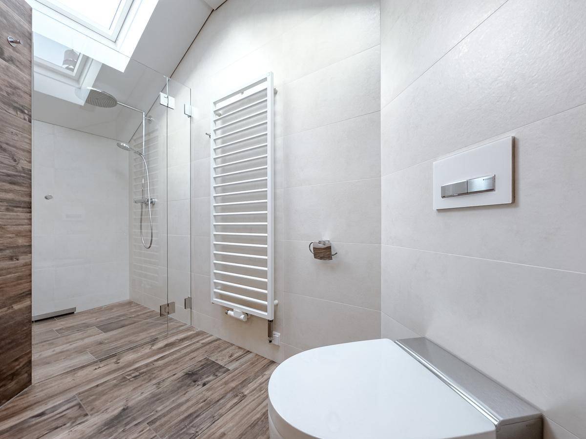 Duschbereich im modernen Badezimmer mit Glasabtrennung, Handtuchheizkörper und Dachfenster.
