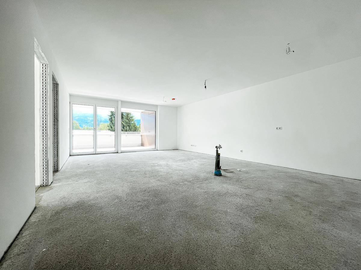 Geräumiger Wohnbereich im Rohbau mit großen Schiebetüren zum Balkon und Blick auf die Berge.