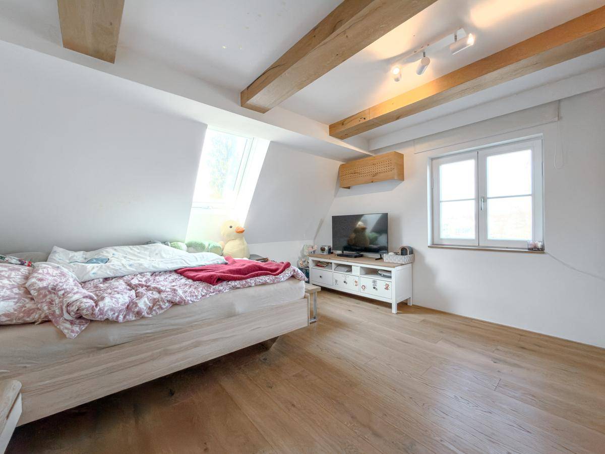 Helles Schlafzimmer im Dachgeschoss mit Holzbalken, Dachfenster und Holzboden.
