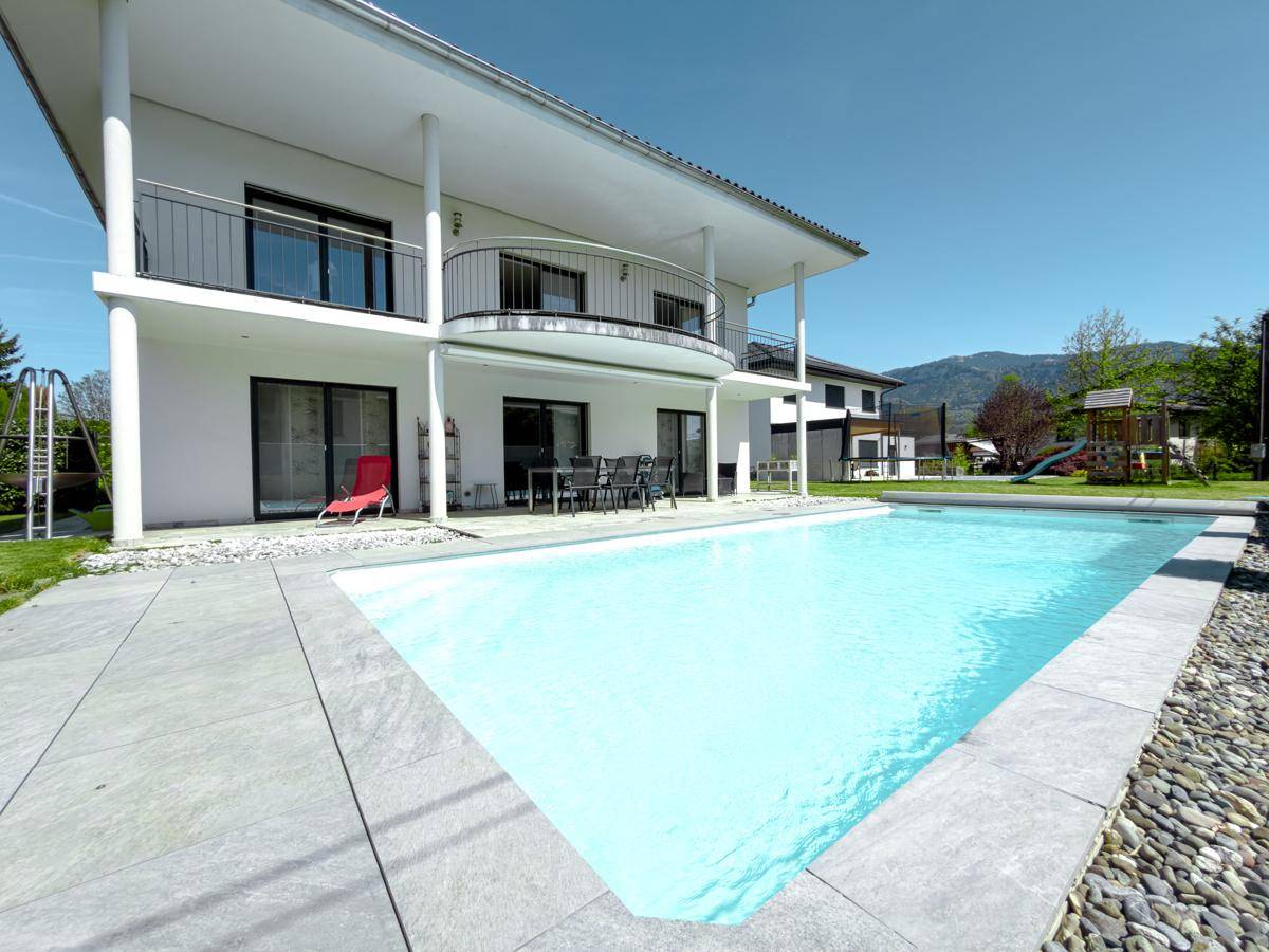 Poolbereich mit großzügiger Terrasse und Blick auf die moderne Architektur des Hauses.