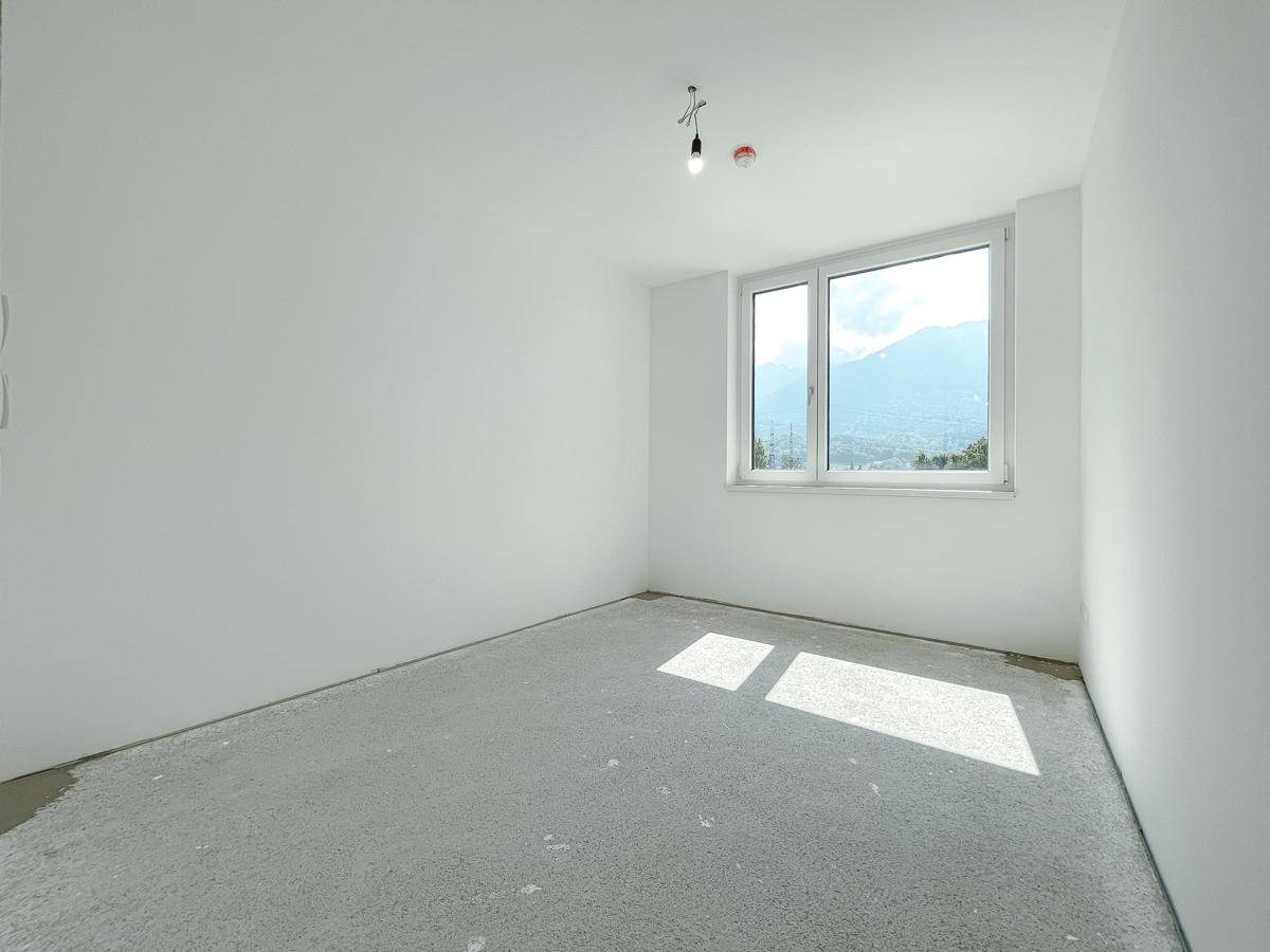 Heller Raum im Rohbau mit Fenster und beeindruckendem Bergblick, bereit für die individuelle Gestaltung.