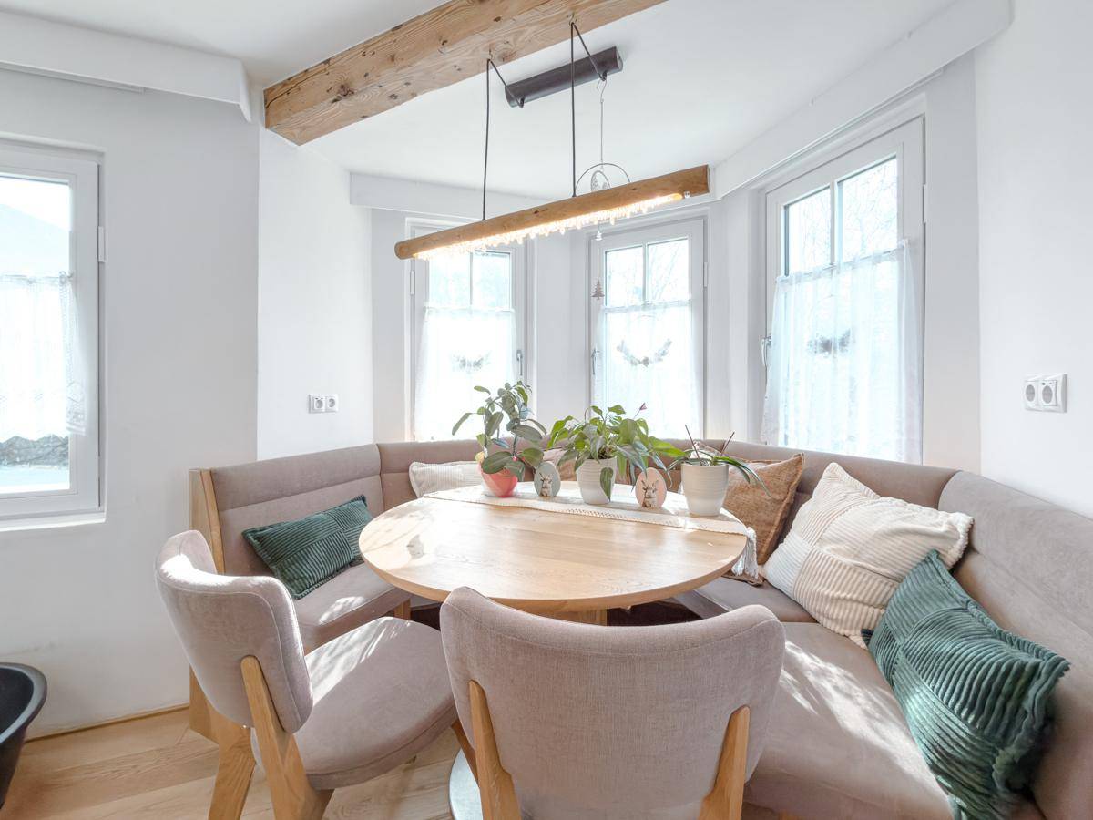 Heller Essbereich mit Holztisch, Eckbank und großen Fenstern, die viel Tageslicht hereinlassen.