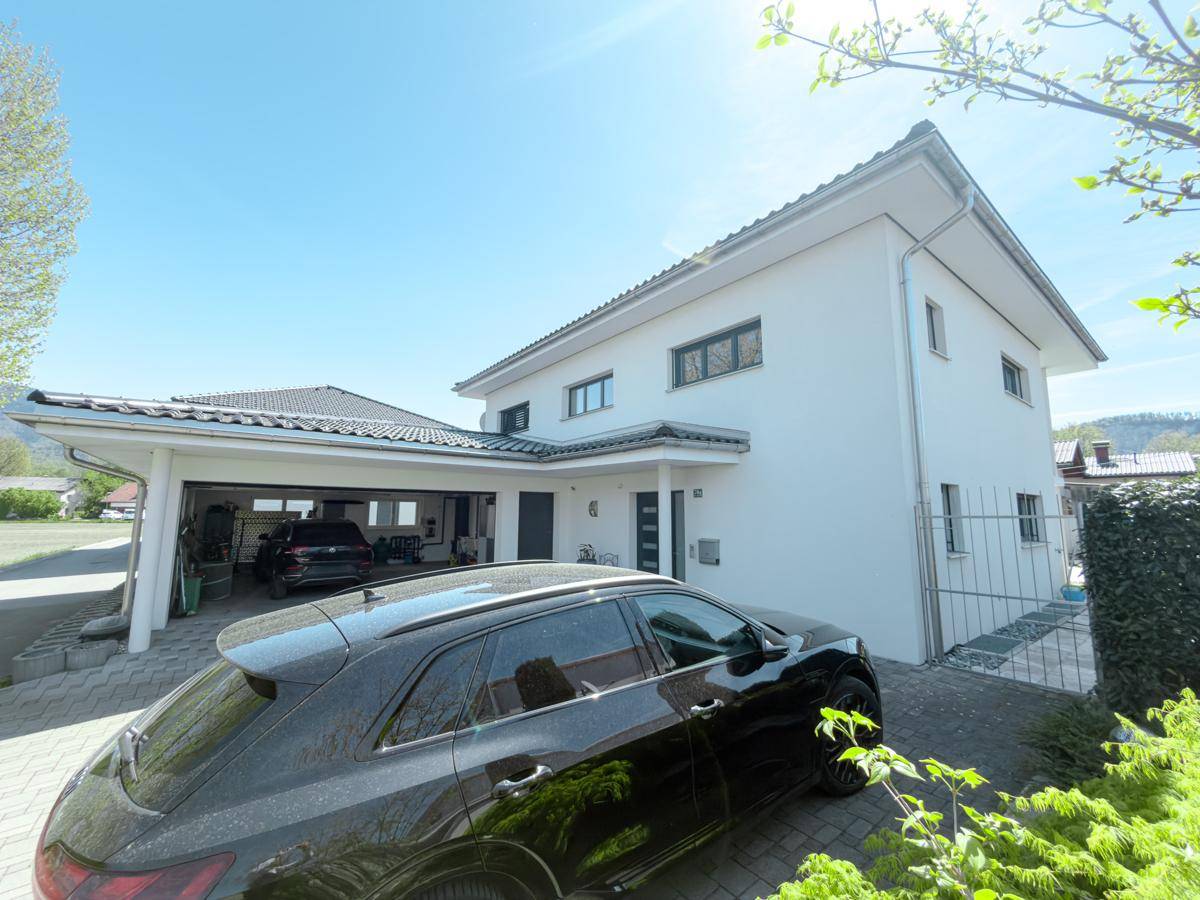 Modernes Einfamilienhaus mit Carport und gepflegter Auffahrt an einem sonnigen Tag.