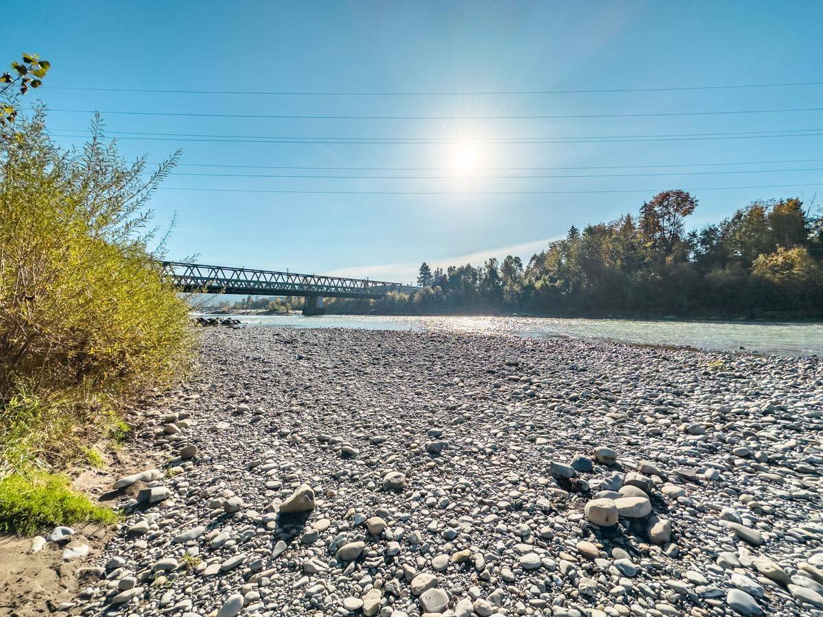 Breiter Fluss mit Kiesufer und Brücke im Hintergrund an einem sonnigen Tag.