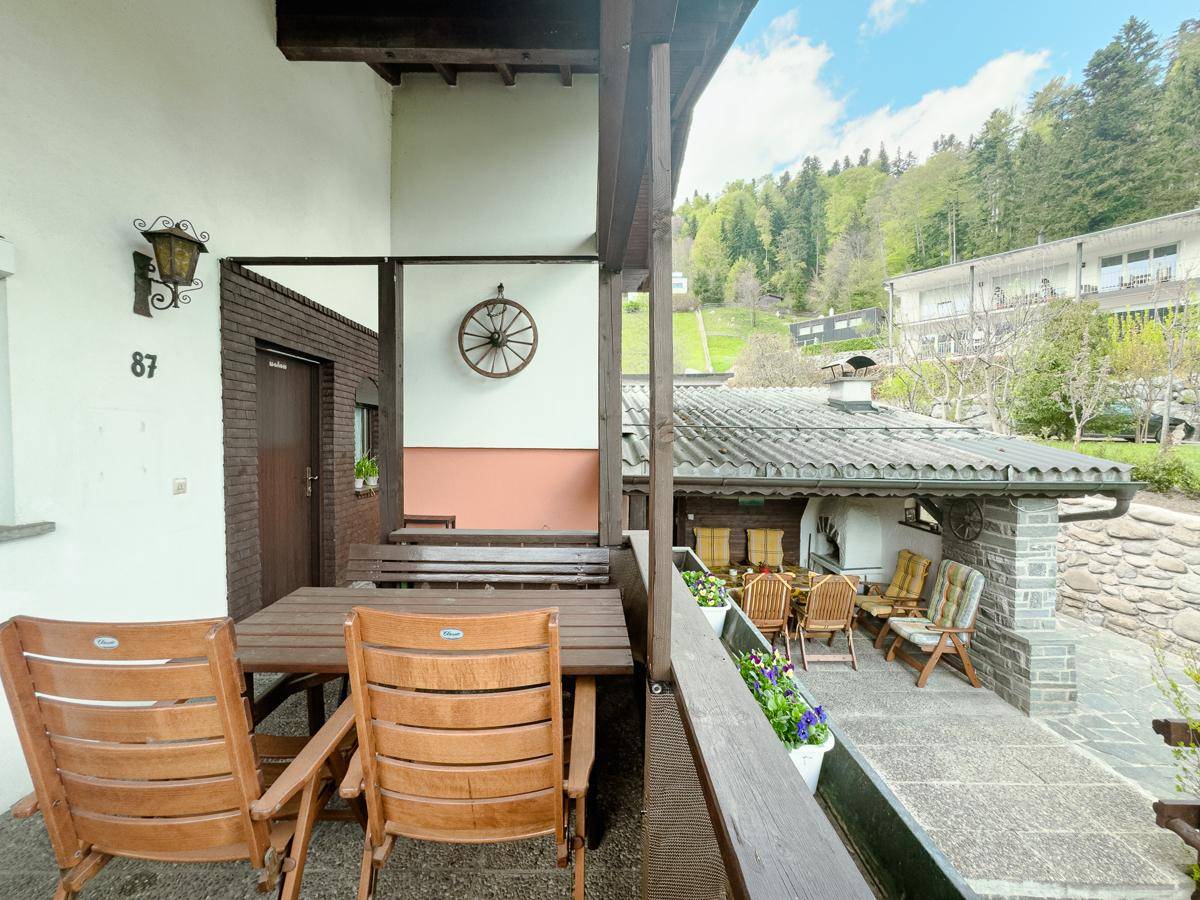 Überdachte Terrasse mit Holztisch und Stühlen, bietet einen schönen Blick auf die umliegende Landschaft.