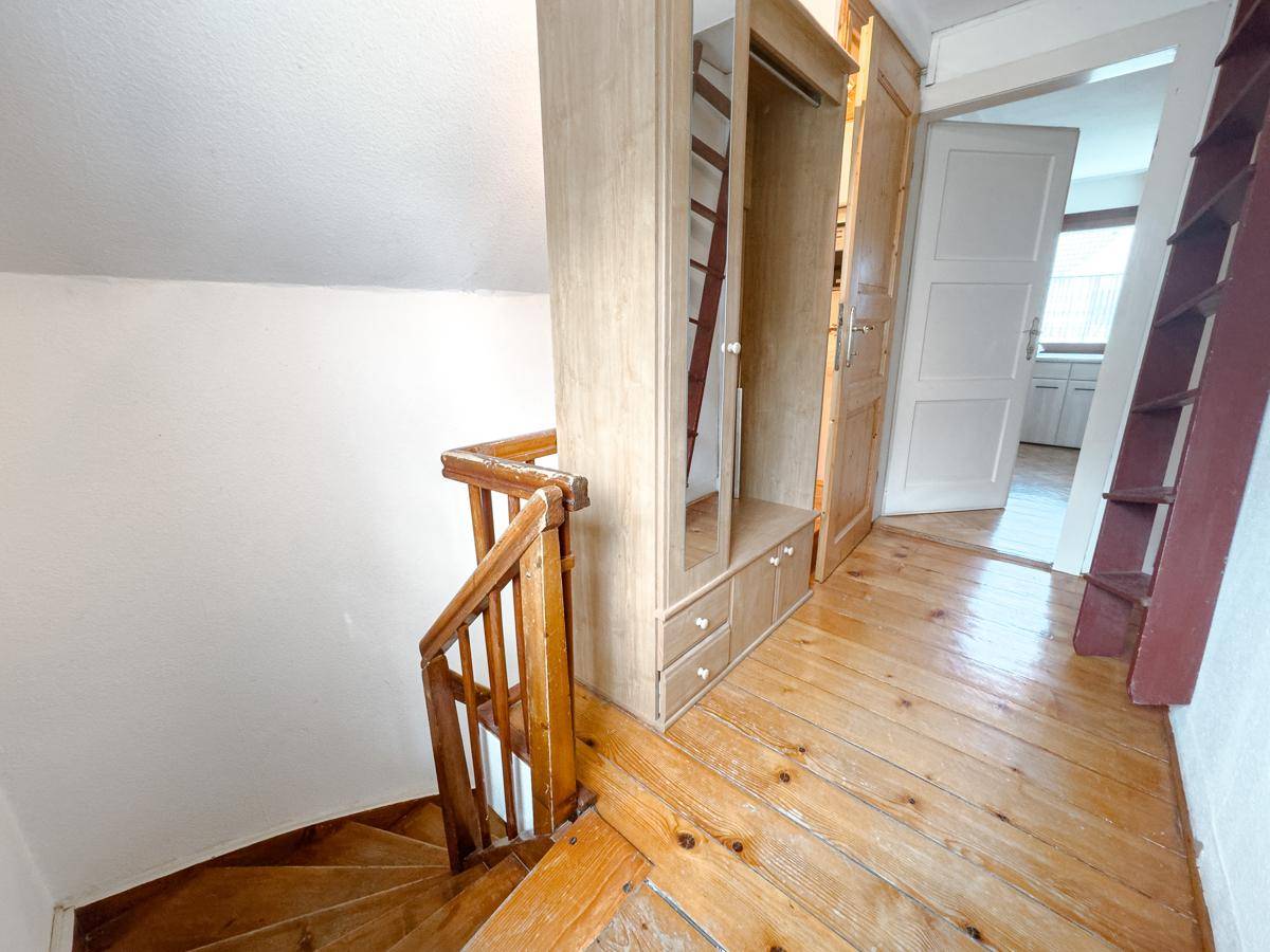 Dachgeschossflur mit Holztreppe, Holzboden und Einbauschrank, der zum Schlafbereich führt.
