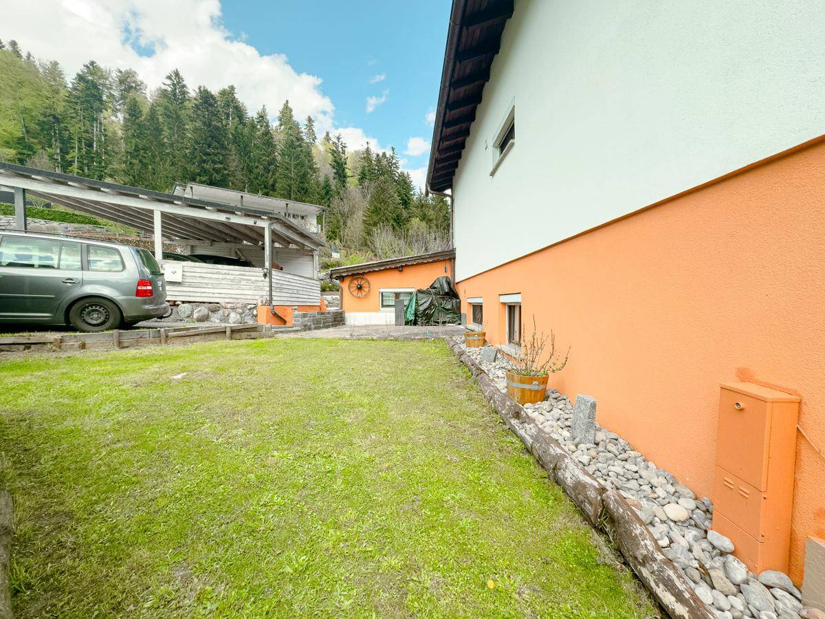 Gartenbereich mit Rasen und Steindekorationen entlang der Hauswand mit orangefarbener Fassade.