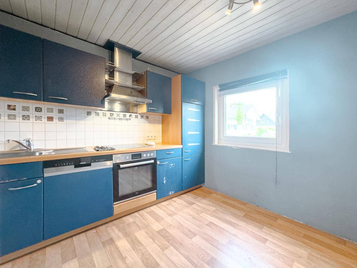 Blaue Einbauküche mit Fenster, integrierten Geräten und Laminatboden.