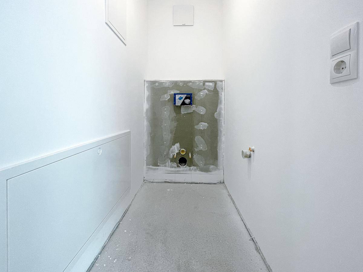 Kleiner Raum im Rohbau, vorbereitet für die Installation einer Toilette, mit weißen Wänden.