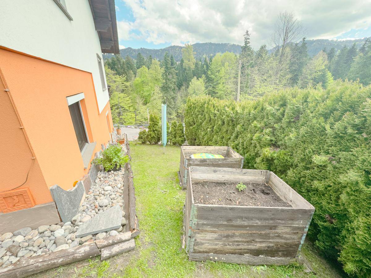Garten mit Hochbeeten und Rasenfläche neben dem Haus mit orangefarbener Fassade.