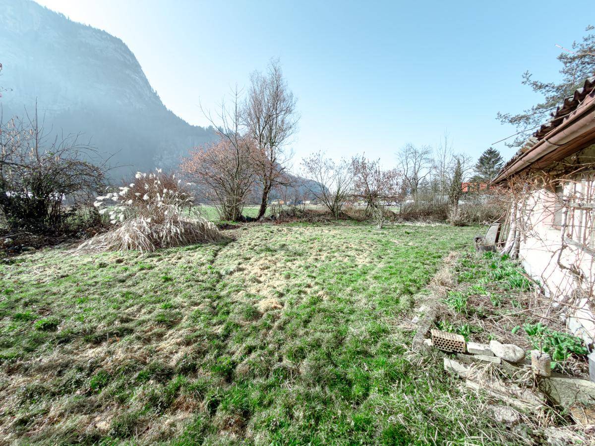 Seitenansicht eines Gebäudes mit angrenzender, ungenutzter Grünfläche und Bergblick.