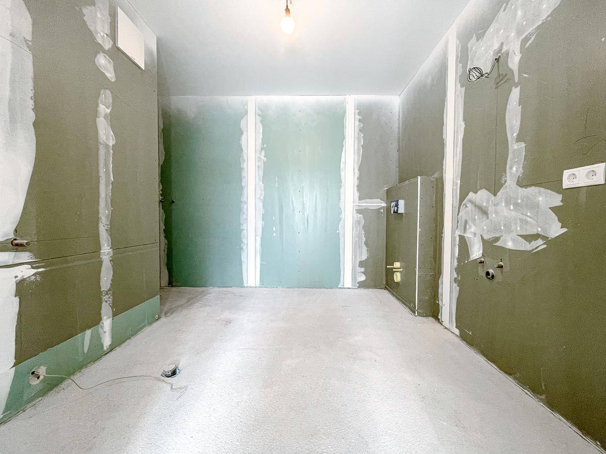 Raum im Rohbauzustand mit Trockenbauwänden und Estrichboden, bereit für den weiteren Ausbau.