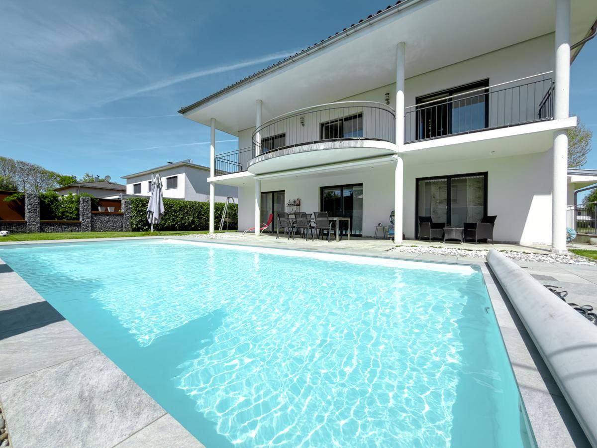 Großer Poolbereich mit gepflasterter Terrasse und Blick auf die moderne Hausfassade.
