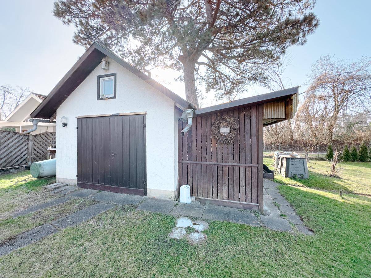 Kleines Nebengebäude mit Garage und Holzunterstand im Gartenbereich.