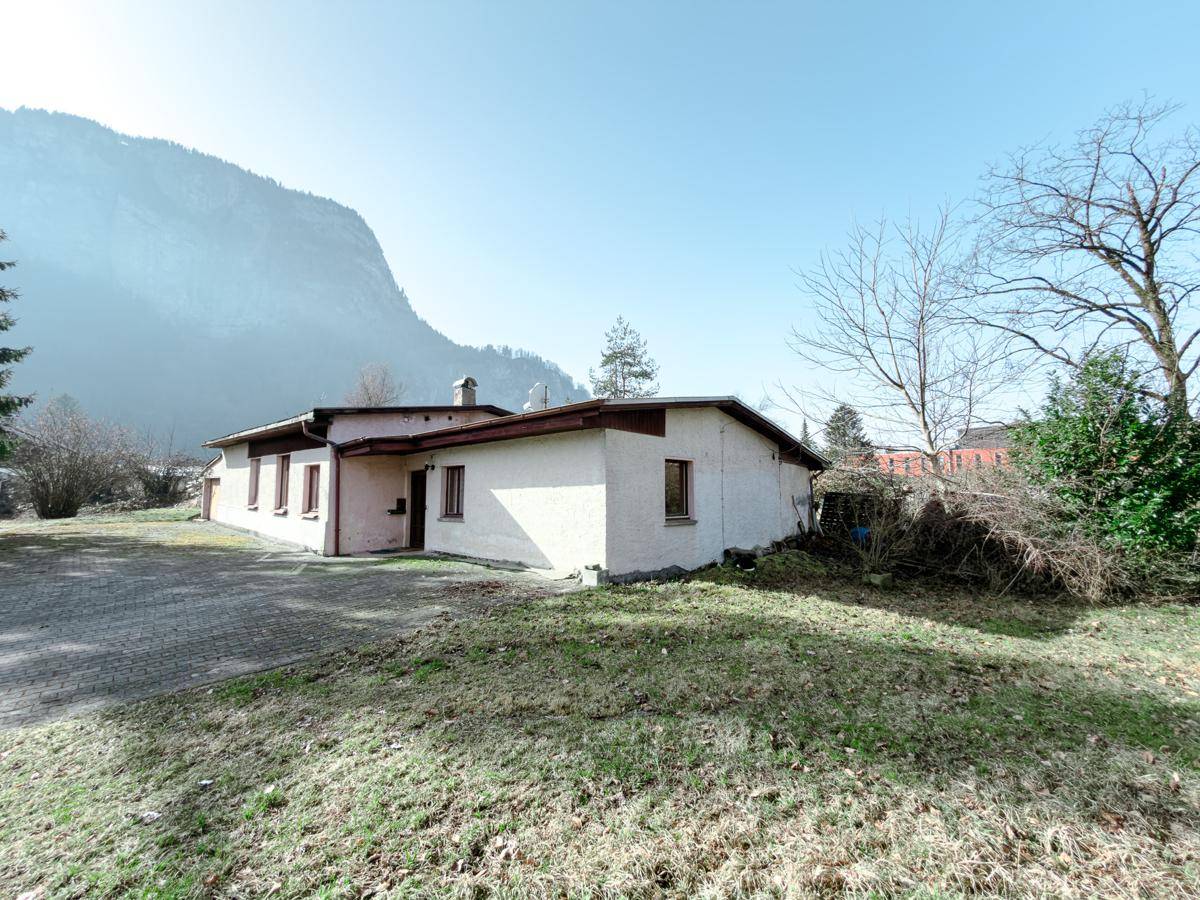 Seitenansicht eines einfachen Gebäudes mit heller Fassade und Bergblick.