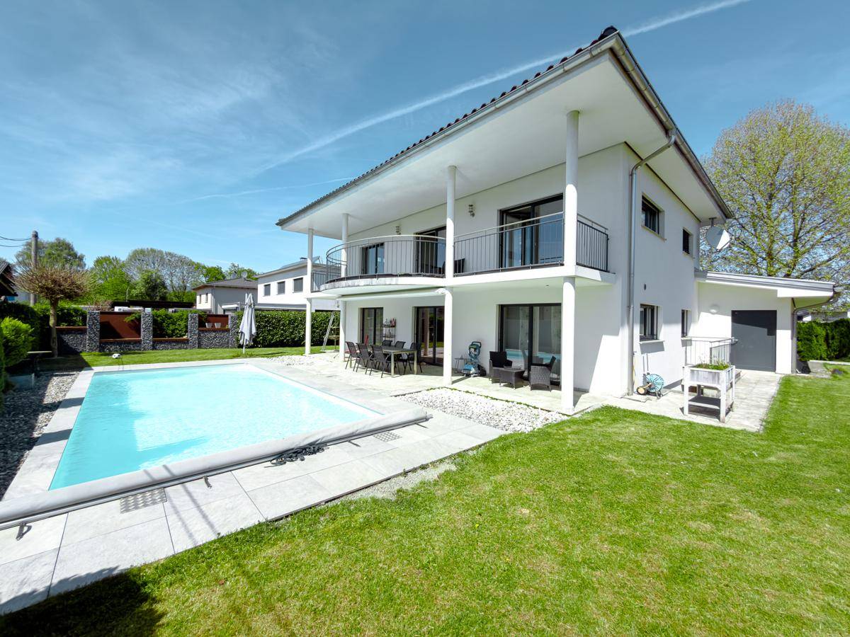 Hinteransicht des Hauses mit großem Pool und gepflasterter Terrasse im Sonnenschein.