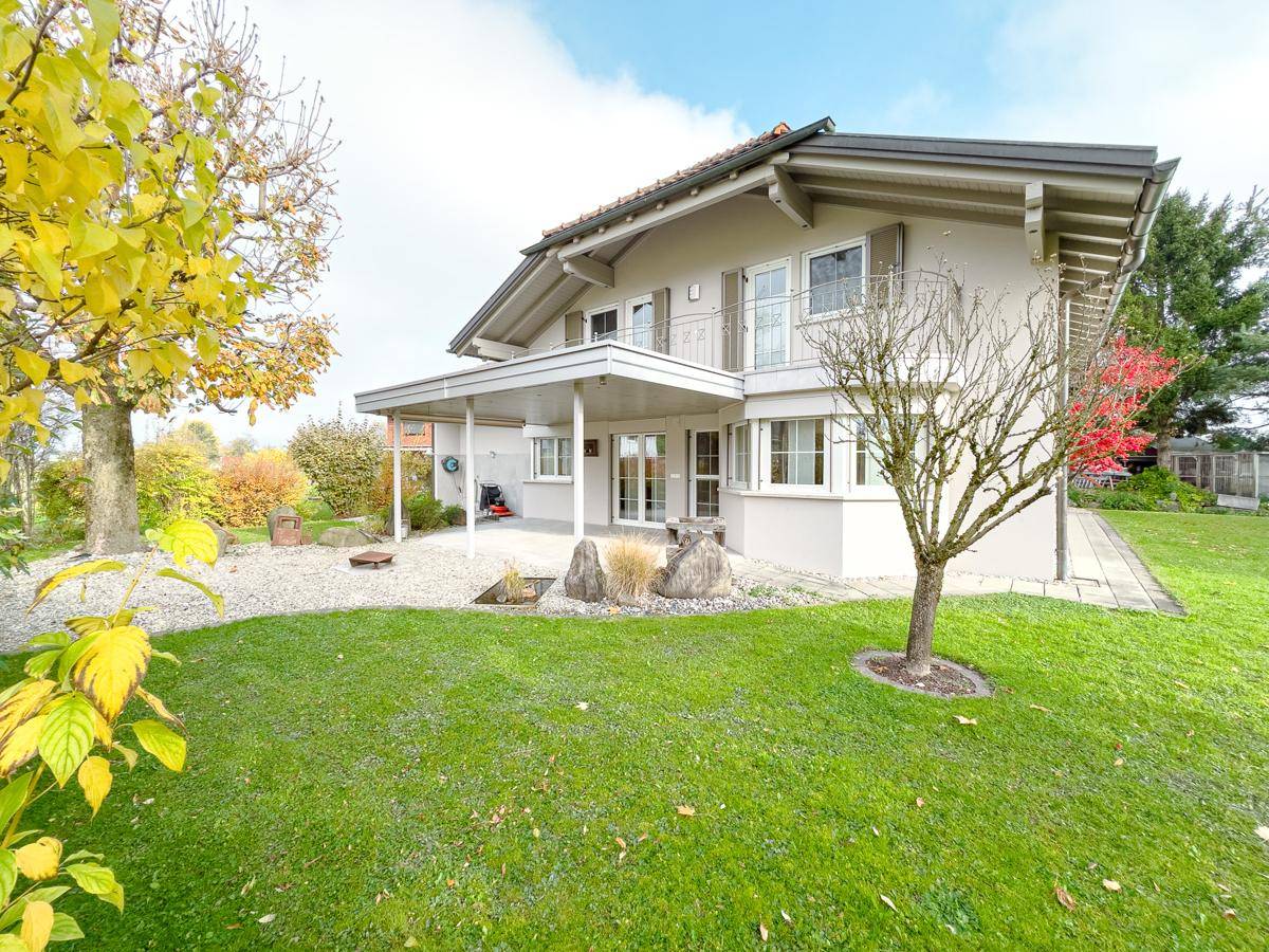 Rückseite des Hauses mit gepflegtem Rasen, Bäumen und einer überdachten Terrasse.