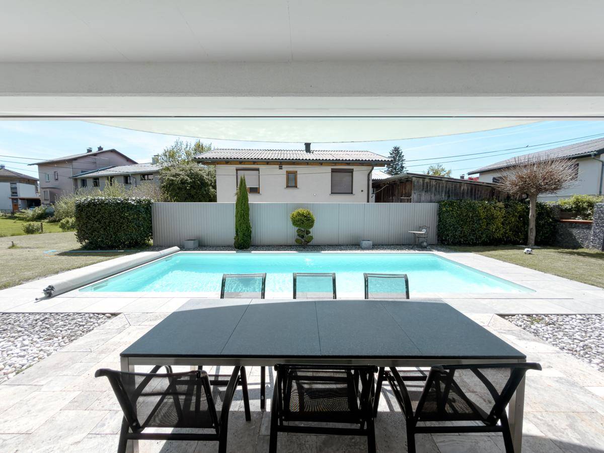 Überdachte Terrasse mit Esstisch und Stühlen, direkt am Pool mit Gartenblick.