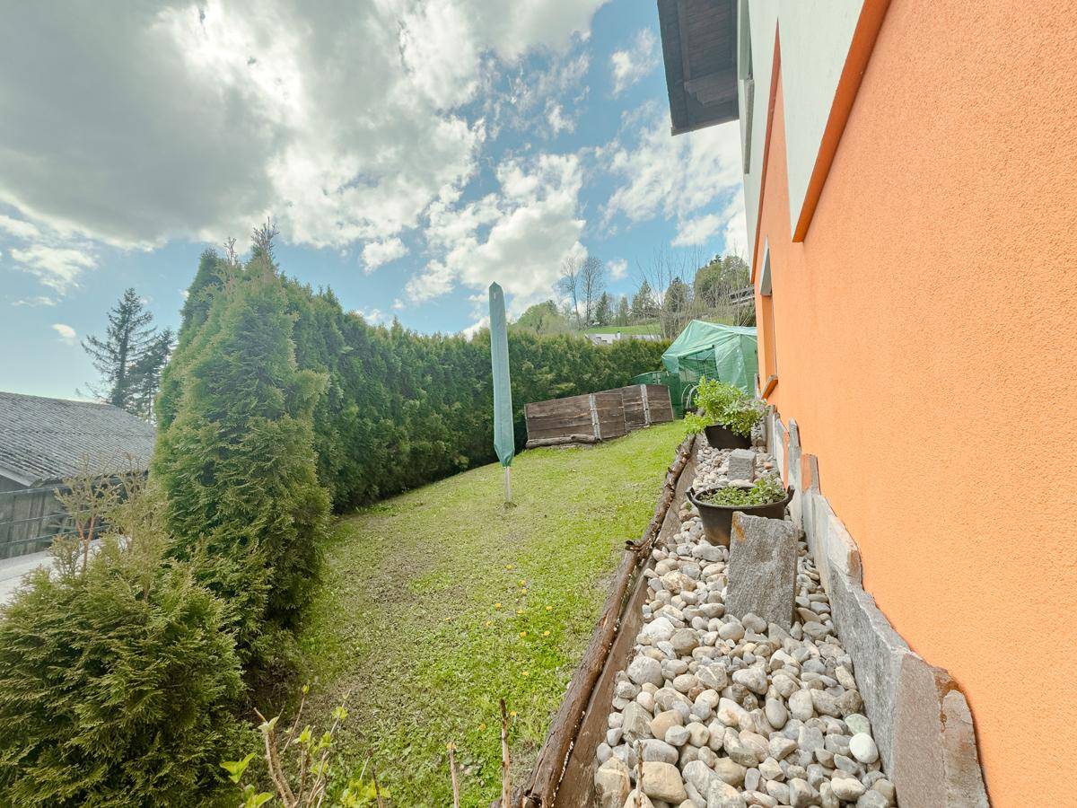 Hanglage-Garten mit Rasen, Hecke und Steindekorationen entlang der Hauswand.