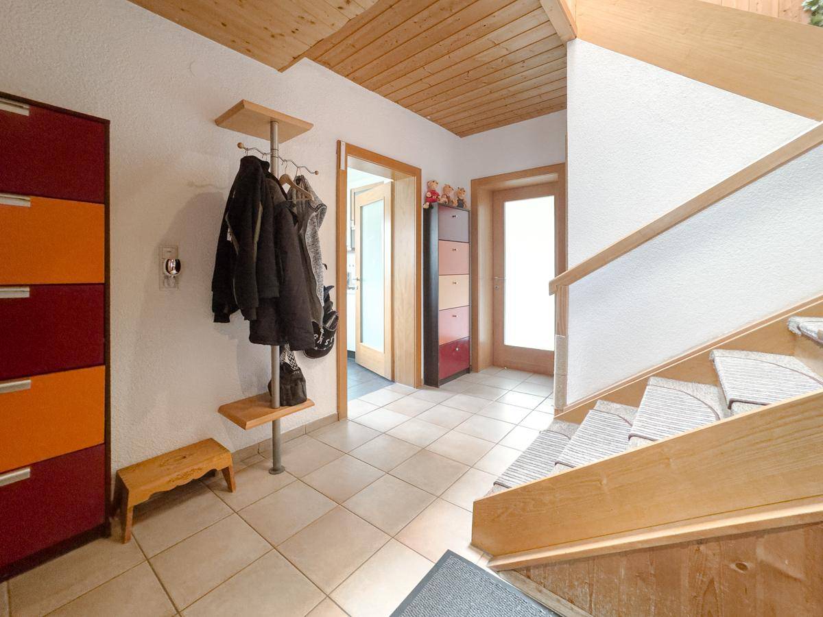 Eingangsbereich mit Fliesenboden, Garderobe und Holztreppe zum Obergeschoss.