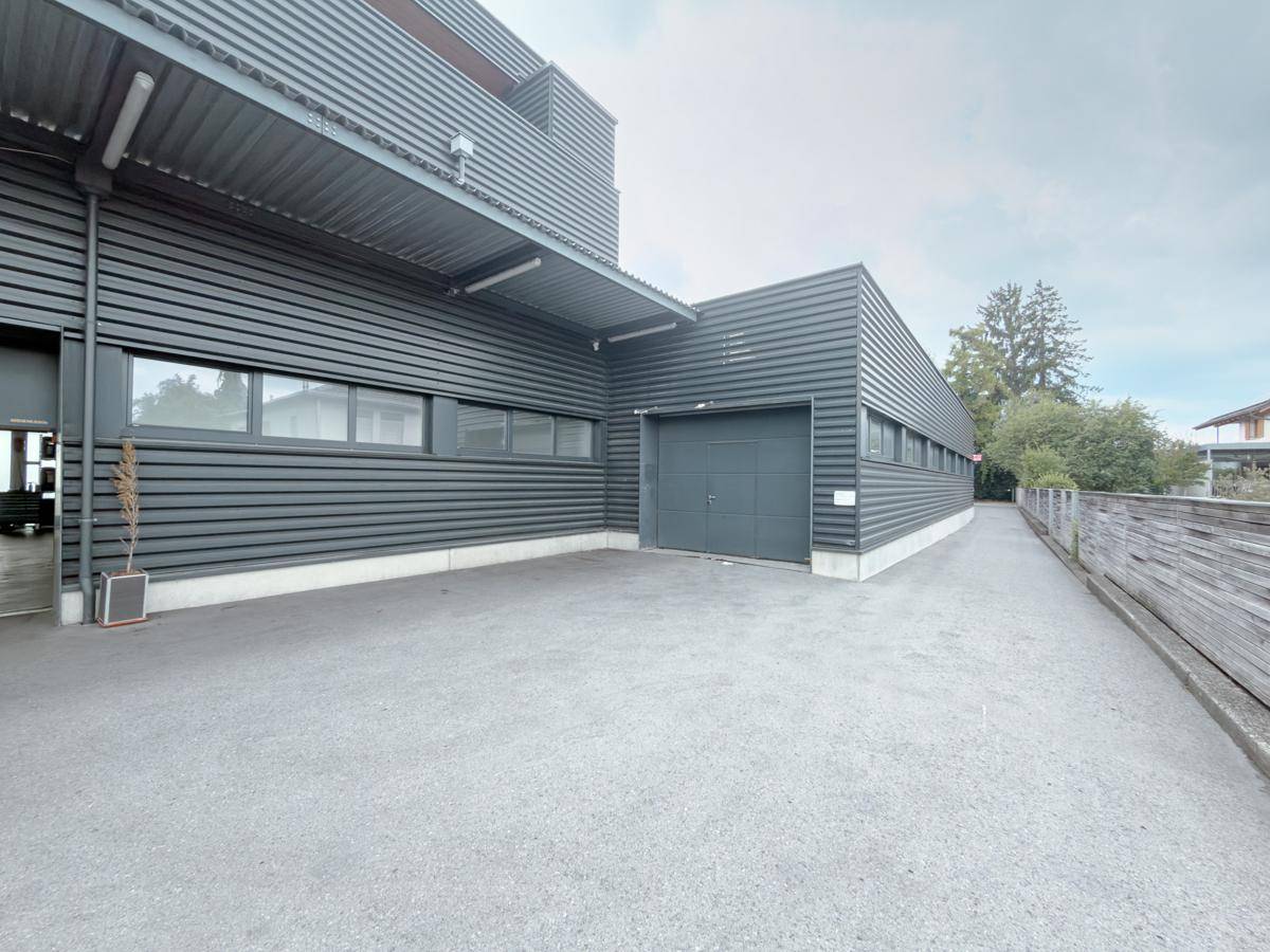 Außenansicht eines modernen Industriegebäudes mit dunkler Fassade und großem Garagentor.