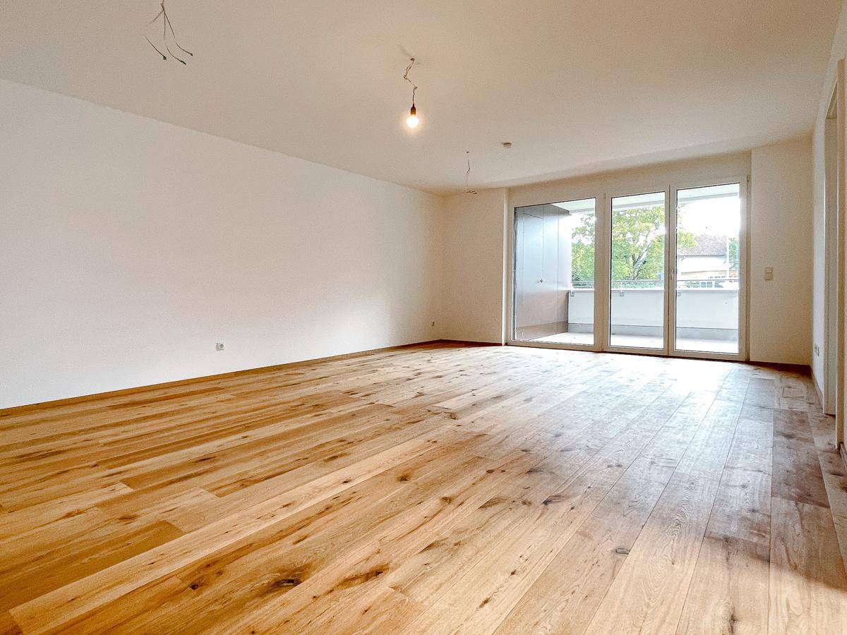 Geräumiges, helles Wohnzimmer mit Echtholzparkett und Zugang zu einem großen Balkon.