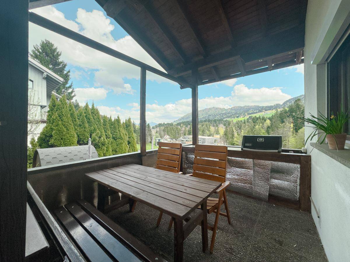 Überdachter Balkon mit Holztisch und Bänken, bietet einen weiten Blick auf die grüne Umgebung.