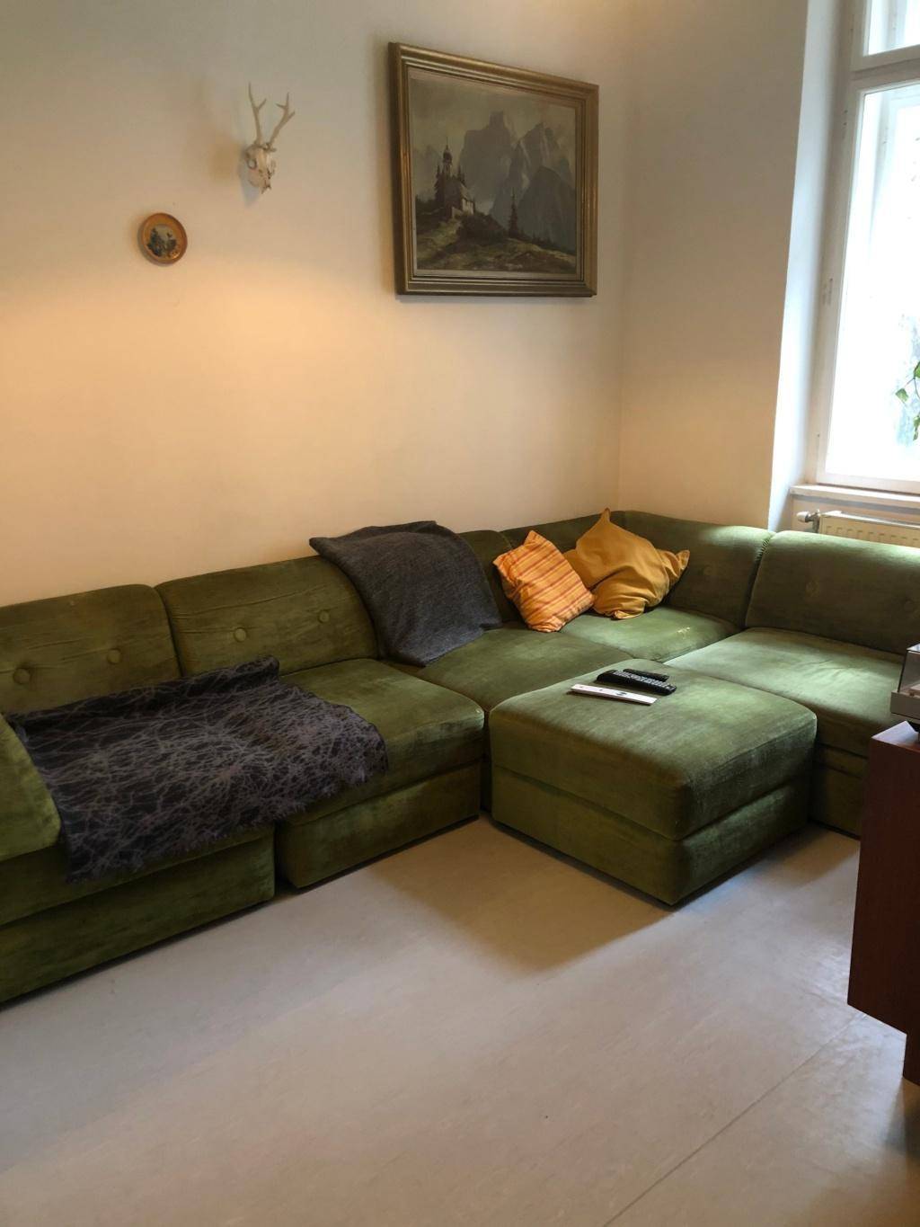 Gemütliches Wohnzimmer mit großem grünem Ecksofa und hellem Boden, ideal zum Entspannen.