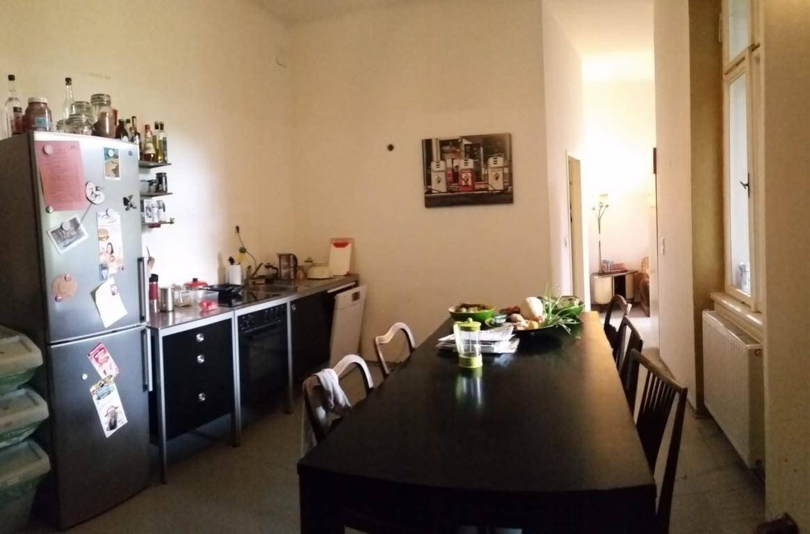 Einfache Küche mit langem Esstisch und Kühlschrank, ideal für gemeinsame Mahlzeiten und geselliges Beisammensein.