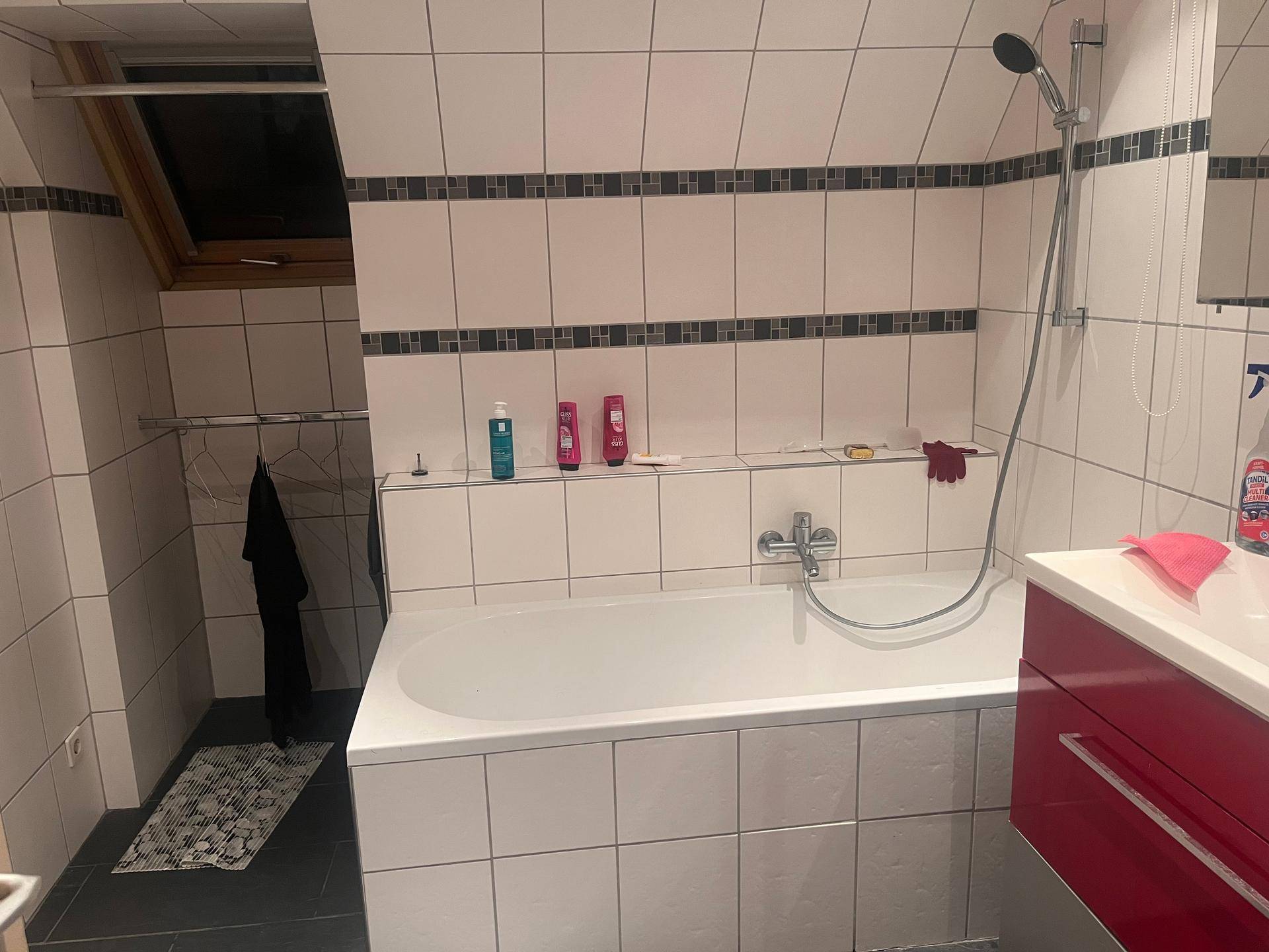 Gefliestes Badezimmer mit Badewanne, Duschvorrichtung, Waschbecken und Dachfenster.