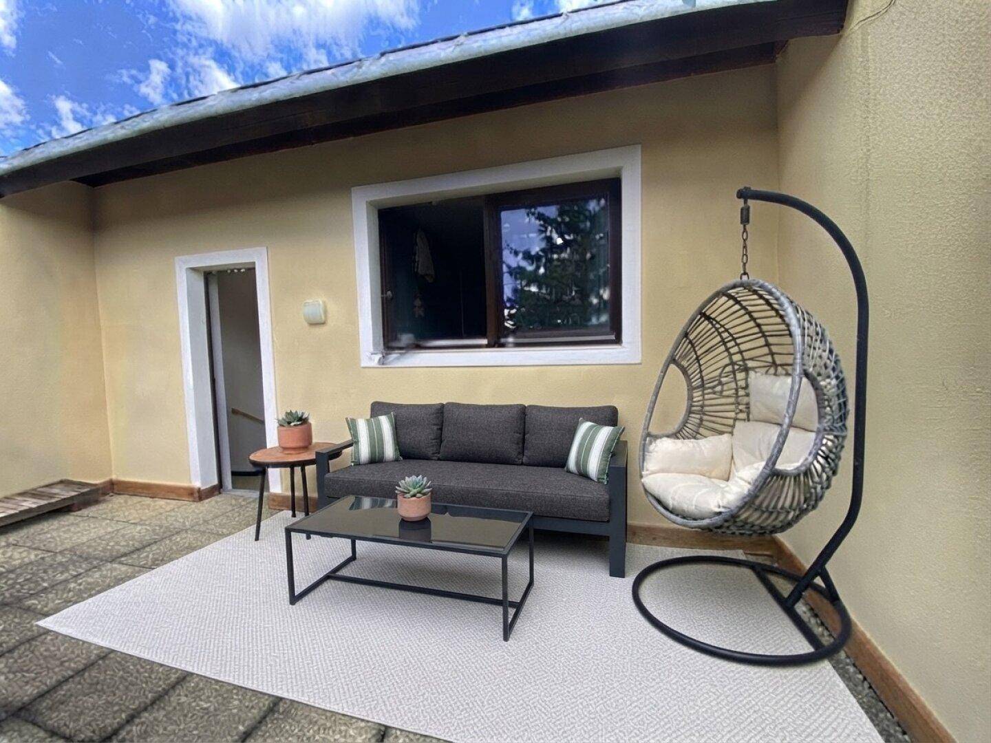 Gemütliche Terrasse mit bequemen Gartenmöbeln und einer Hängeschaukel, ideal zum Entspannen im Freien.