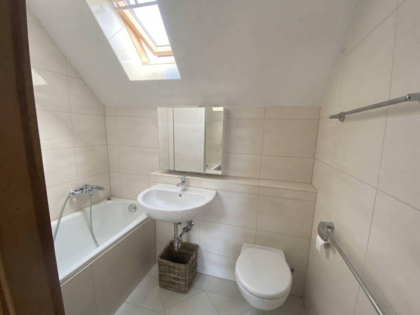 Badezimmer mit Badewanne, Waschbecken, WC und einem Dachfenster, das für natürliches Licht sorgt.