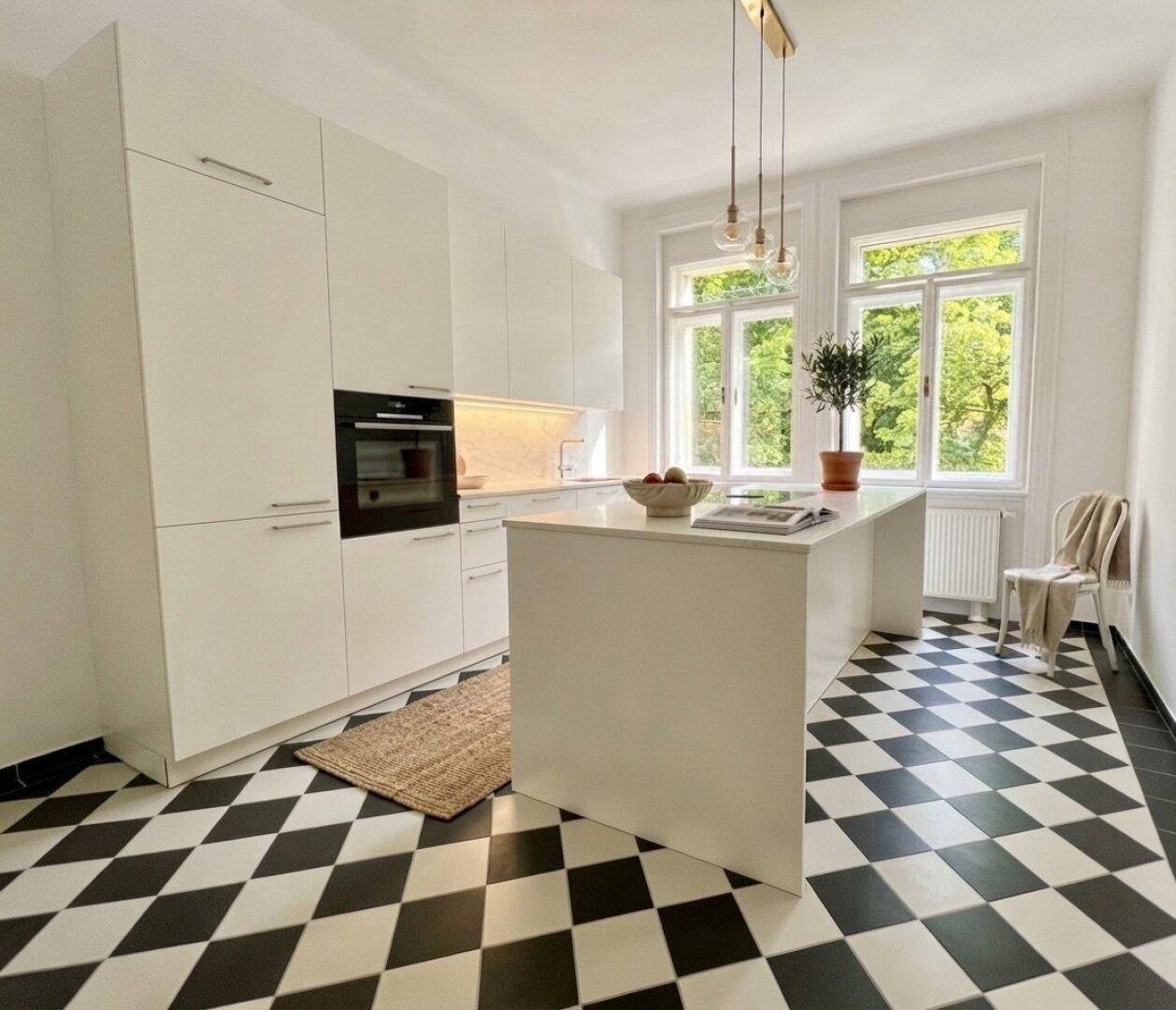 Moderne weiße Küche mit Kochinsel, schwarz-weißem Fliesenboden und großen Fenstern.