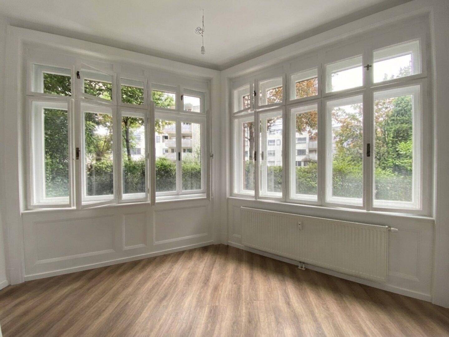 Helles Zimmer mit vielen Fenstern, Laminatboden und Blick ins Grüne.